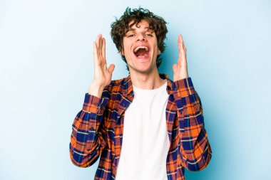 Mavi arka planda izole olmuş genç beyaz adam yüksek sesle gülüyor ve elini göğsüne koyuyor..