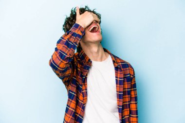 Mavi arka planda izole edilmiş genç beyaz adam ellerini başının üstünde tutarak neşe içinde gülüyor. Mutluluk kavramı.