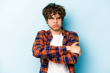 Mavi arka planda izole edilmiş genç beyaz adam omuzlarını silkeliyor ve gözleri açık..