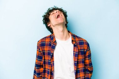 Kafkasyalı genç adam mavi arka planda izole edilmiş rahat ve mutlu bir şekilde gülüyor, boynunda dişlerini gösteriyor..