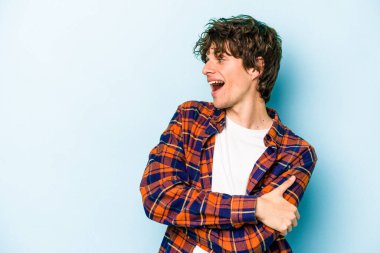 Mavi arka planda izole edilmiş genç beyaz adam kollarını kavuşturarak gülümsüyor..