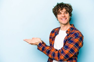 Mavi arka planda izole edilmiş genç beyaz bir adam palmiyesinde bir kopya alanı tutuyor..