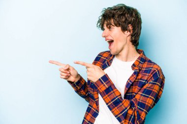 Kafkasyalı genç adam mavi arka plan noktalarında izole edilmiş başparmak uzakta, gülüyor ve kaygısız.