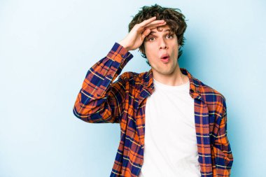 Kafkasyalı genç adam mavi arka planda izole edilmiş, uzaklara bakıyor ve elini alnına koyuyor..