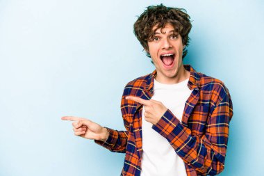 Kafkasyalı genç adam mavi arka planda izole edilmiş. İşaret parmağıyla işaret ettiği için heyecanlı..