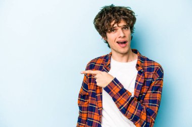 Mavi arka planda izole edilmiş genç beyaz adam yan tarafı işaret ediyor.