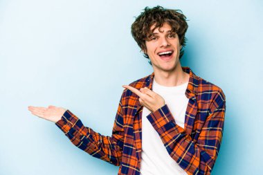 Kafkasyalı genç adam mavi arka planda izole edilmiş. Elinde palmiye ağacının bir kopyası olduğu için heyecanlı..