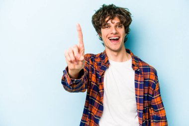 Mavi arka planda izole edilmiş genç beyaz adam bir numarayı parmağıyla gösteriyor..