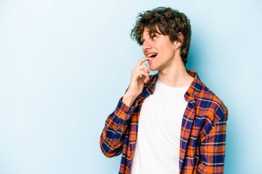 Mavi arka planda izole edilmiş genç beyaz adam rahatlamış bir şeyin fotokopi odasına baktığını düşünüyor..