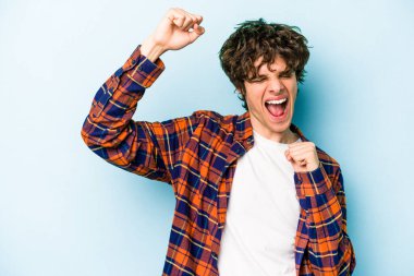 Mavi arka planda izole edilmiş genç beyaz bir adam zaferden sonra yumruğunu kaldırıyor, kazanan konsept..