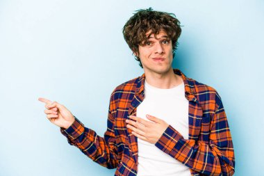 Mavi arka planda izole edilmiş genç beyaz adam işaret parmağıyla fotokopi alanını işaret ederek şok oldu..