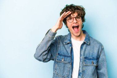 Mavi arka planda izole edilmiş genç beyaz adam yüksek sesle bağırıyor, gözleri açık ve elleri gergin tutuyor..