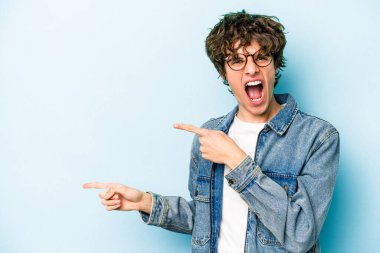 Mavi arka planda izole edilmiş genç beyaz adam işaret parmağıyla fotokopi alanını işaret ederek heyecan ve arzusunu ifade ediyor..