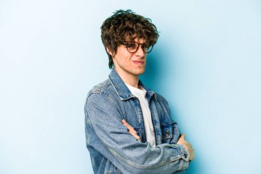 Kafkasyalı genç adam mavi arka planda izole edilmiş hoşnutsuzca kaşlarını çatmış, kollarını kavuşturmuş..