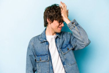 Kafkasyalı genç adam mavi arka planda izole edilmiş bir şekilde bir şeyi unutuyor. Alnına avuç içi ve gözlerini kapayarak vuruyor..