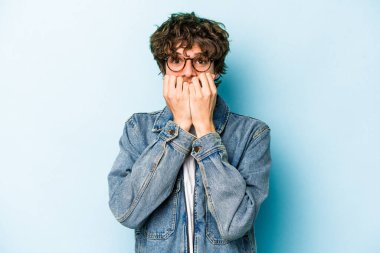 Mavi arka planda izole edilmiş, tırnak yiyen, gergin ve endişeli genç bir beyaz adam..