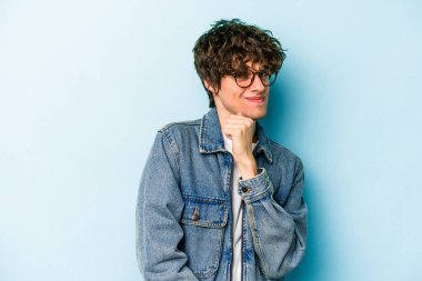 Kafkasyalı genç adam mavi arka planda izole, kafası karışmış, şüpheli ve güvensiz hissediyor..