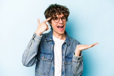 Mavi arka planda izole edilmiş genç beyaz adam işaret parmağıyla bir hayal kırıklığı jesti gösteriyor..