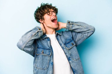 Kafkasyalı genç adam mavi arka planda izole edilmiş. Kendine güveniyor, elleri başının arkasında..