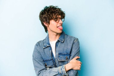 Kafkasyalı genç adam mavi arka planda izole edilmiş komik ve dost canlısı bir dil uzatıyor..