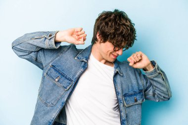 Mavi arka planda izole edilmiş genç beyaz adam kollarını uzatıyor, rahat bir konumda..