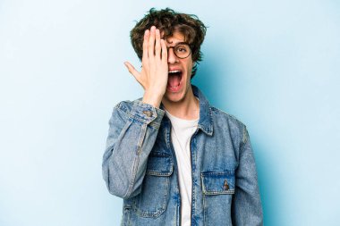 Mavi arka planda izole edilmiş genç beyaz adam yüzünün yarısını palmiye ile kaplayarak eğleniyor..