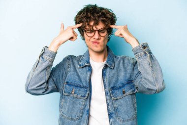 Kafkasyalı genç adam mavi arka planda izole edilmiş bir göreve odaklanmış, parmaklarını işaret ediyor..