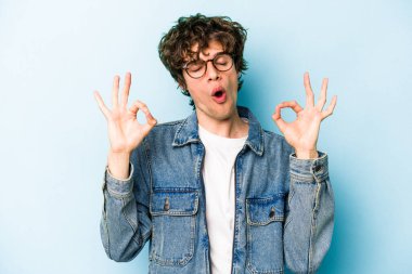 Mavi arka planda izole edilmiş genç beyaz adam yorucu bir günün ardından rahatlıyor. Yoga yapıyor..