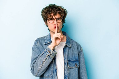 Mavi arka planda izole edilmiş genç beyaz bir adam ya sır saklıyor ya da sessizlik istiyor..