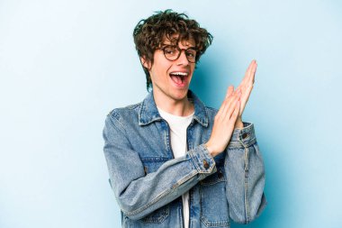 Kafkasyalı genç adam mavi arka planda izole edilmiş enerjik ve rahat hissediyor, ellerini ovuşturuyor kendinden emin.