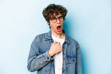 Mavi arka planda izole edilmiş genç beyaz adam parmağını göstererek şaşırdı, geniş bir gülümsemeyle..