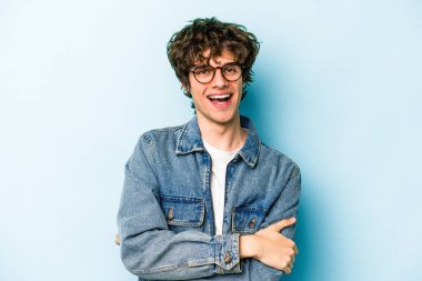 Mavi arka planda kendini güvende hisseden, kararlılıkla kollarını kavuşturan genç beyaz bir adam..