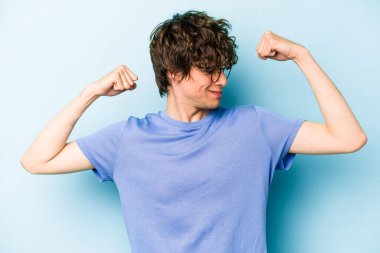 Mavi arka planda izole edilmiş genç beyaz adam güçlü bir hareket sergiliyor kollarıyla, kadınsı gücün sembolü.