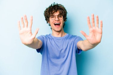Mavi arka planda izole edilmiş genç beyaz adam on numarayı elleriyle gösteriyor..