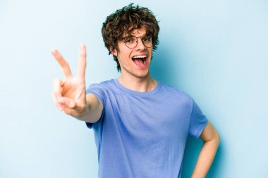 Kafkasyalı genç adam mavi arka planda izole edilmiş neşeli ve kaygısız parmaklarıyla barış sembolü gösteriyor..