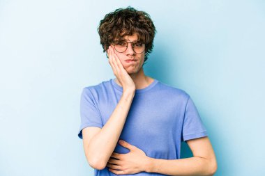 Mavi arka planda izole edilmiş genç beyaz adamın yanakları şişer, yorgun bir ifadesi vardır. Yüz ifadesi kavramı.