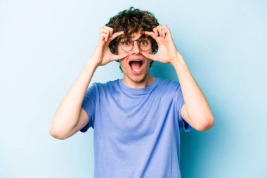 Mavi arka planda izole edilmiş genç beyaz adam bir başarı fırsatı bulmak için gözlerini açık tutuyor..