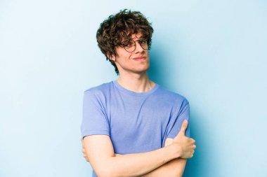 Mavi arka planda izole edilmiş genç beyaz adam alaycı bir ifadeyle kameraya bakarken mutsuz oluyor..