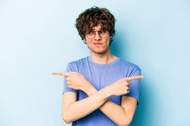 Mavi arka plan noktalarında izole genç beyaz adam, iki seçenek arasında seçim yapmaya çalışıyor.