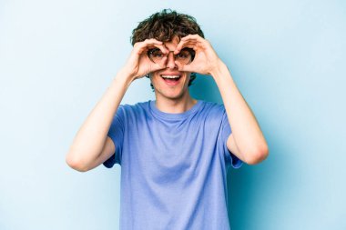 Mavi arka planda izole edilmiş genç beyaz adam gözlerinde sorun olmadığını gösteriyor.