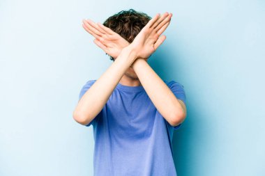 Kafkasyalı genç adam mavi arka planda izole edilmiş iki kolu çapraz tutuyor, inkar kavramı.