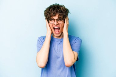 Kafkasyalı genç adam mavi arka planda izole edilmiş kulakları kulaklarıyla kapatıyor çok fazla ses duymamaya çalışıyor..