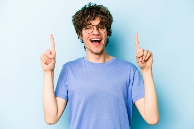 Mavi arka planda izole genç beyaz adam işaret iki ön parmakları boş bir boşluk gösteren.