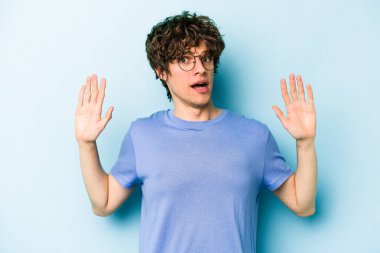 Mavi arka planda izole genç beyaz adam yakın bir tehlike nedeniyle şoka uğruyor