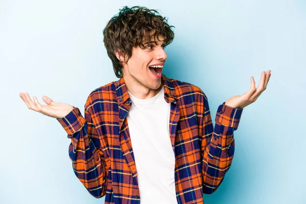 Kafkasyalı genç adam mavi arka planda izole edilmiş neşeli bir şekilde gülüyor. Mutluluk kavramı.