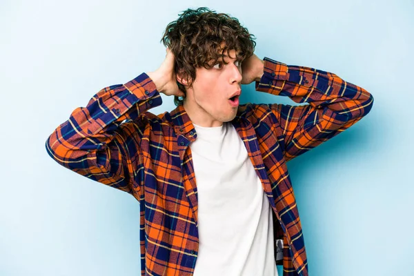 Genç beyaz adam mavi arka planda izole edilmiş bağırıyor, çok heyecanlı, tutkulu, bir şeyden memnun..