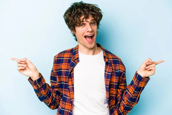 Mavi arka planda izole edilmiş genç beyaz adam farklı kopya alanlarını gösteriyor, birini seçiyor, parmaklarıyla gösteriyor.