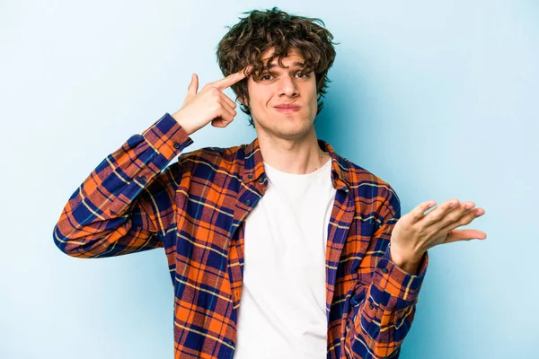 Kafkasyalı genç adam mavi arka planda izole edilmiş ve elinde bir ürün tutuyor..