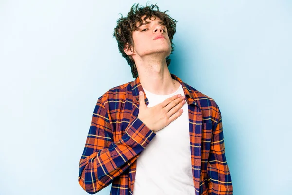 Kafkasyalı genç adam mavi arka planda izole edilmiş yemin ediyor, elini göğsüne koyuyor..