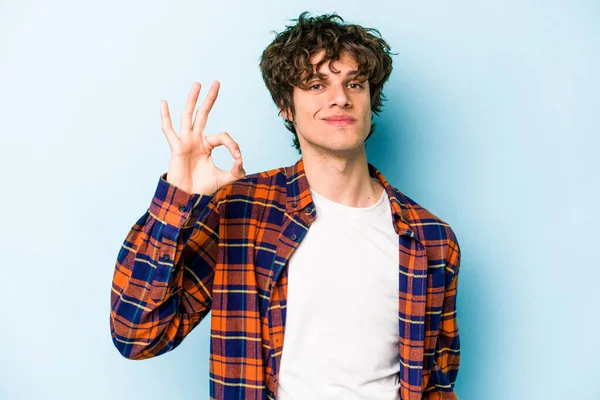 Kafkasyalı genç bir adam mavi arka planda izole edilmiş bir şekilde göz açıp kapayana kadar iyi bir el hareketi yapıyor..